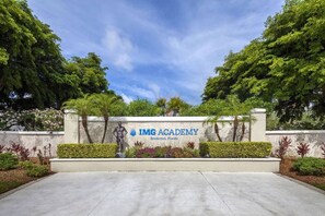 Schild für IMG Academy in Bradenton, Florida, mit einer Statue, Grünflächen und einem wolkenlosen Himmel.