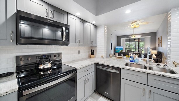 A modern kitchen with stainless steel appliances, grey cabinetry, and a large island with a sink.