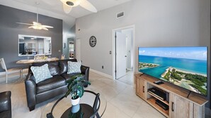 A modern living room with a leather sofa, a coffee table with a plant, a TV on a wooden stand, and a ceiling fan.