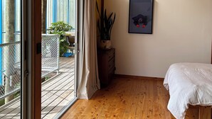 A bedroom with wooden flooring, a bed, a potted plant, a framed picture, and a view of the outdoors through a sliding glass door. - 'The Dogbox' Architectural home in Central Whanganui. (Whanganui)
