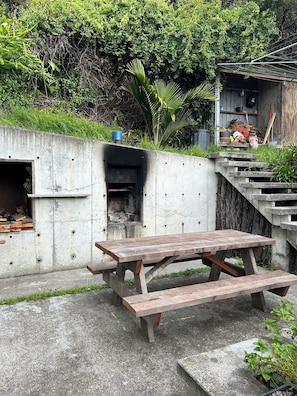 A concrete outdoor area with a picnic table, a small fire pit, and a wooden structure in the background. - 'The Dogbox' Architectural home in Central Whanganui. (Whanganui)