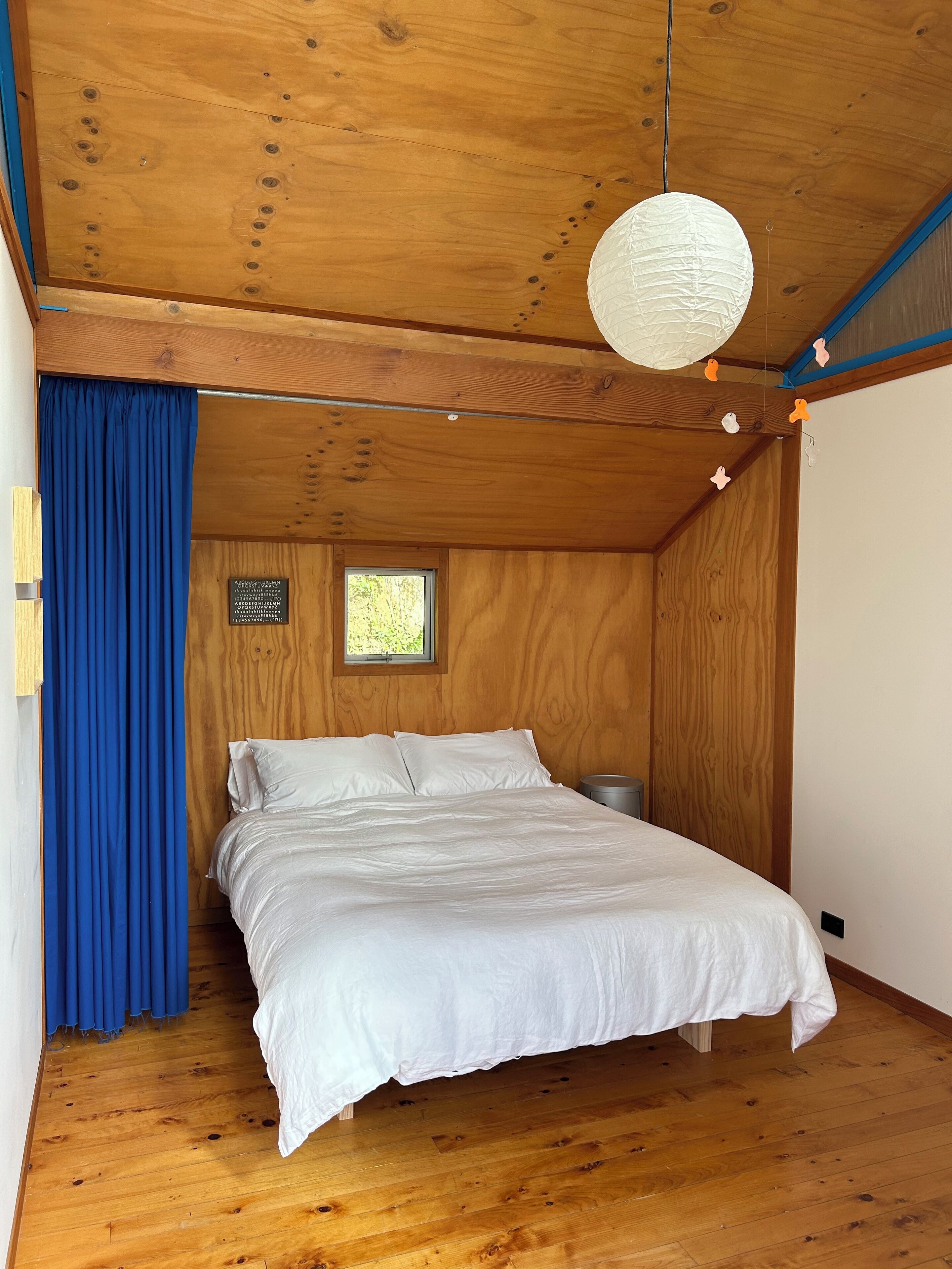 Une pièce en bois avec un lit, une fenêtre et un luminaire suspendu.