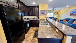 Eine moderne Küche mit dunklen Holzschränken, einem schwarzen Kühlschrank, Granit-Arbeitsplatten und einer integrierten Kochinsel mit Spüle.