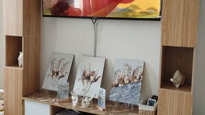 Een moderne woonkamer met een flatscreen televisie bevestigd aan een houten wandmeubel, met een decoratieve plank met ingelijste kunst en een klein tafeltje met een decoratief object.