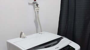 Een compacte, witte Whirlpool waterverwarmer met bedieningspaneel, verbonden met een rood ventiel en een witte slang die aan de muur bevestigd zijn.