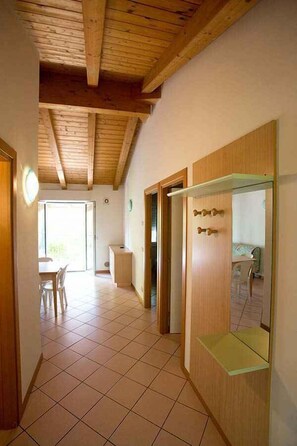 A room with a wooden ceiling, tiled floor, a door with a mirror, and a view to a dining area.