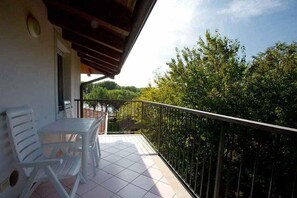 A balcony with a table and chairs, a railing, and a view of trees and sky.