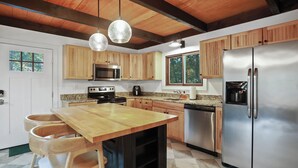 A modern kitchen with wooden cabinets, stainless steel appliances, and a central island with stools. - Modern Chalet with Hot Tub, Fire Pit & Mountain Views in Basye, VA (Basye)