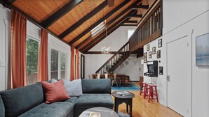 A modern living room with a sectional sofa, a coffee table, and a staircase leading to an upper level. - Modern Chalet with Hot Tub, Fire Pit & Mountain Views in Basye, VA (Basye)