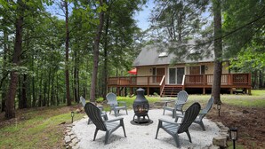 A cabin with a deck, surrounded by trees, featuring a fire pit with chairs. - Modern Chalet with Hot Tub, Fire Pit & Mountain Views in Basye, VA (Basye)