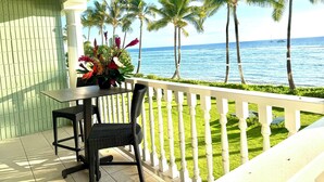 Ein Balkon mit Tisch und Stühlen, einem Blumentopf und Blick auf das Meer und Palmen.