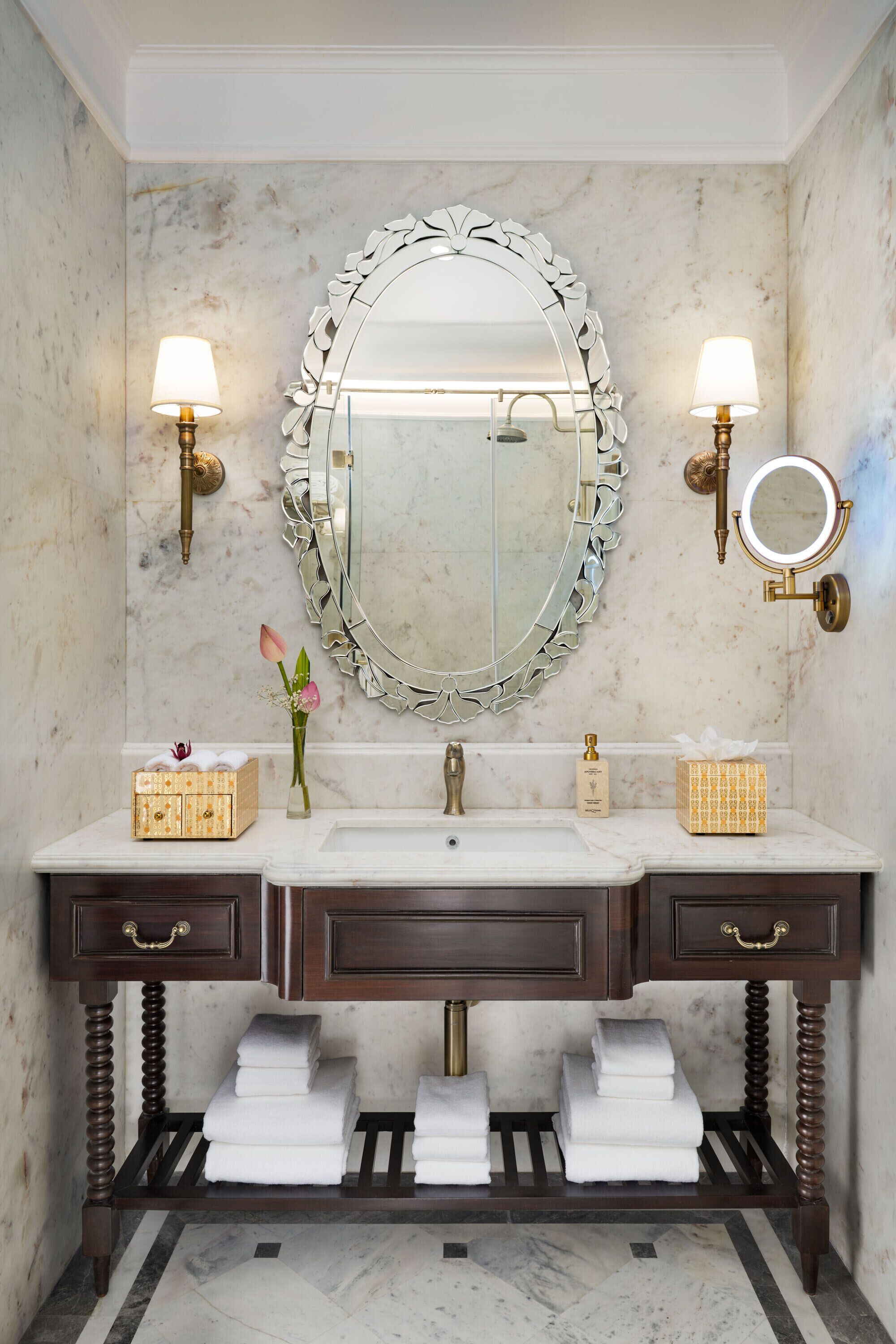 A bathroom with a marble vanity, two wall-mounted lights, a large mirror with a decorative frame, and a small round mirror.
