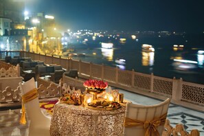 Mesa lista para cenar con vistas a un río y luces de la ciudad por la noche.