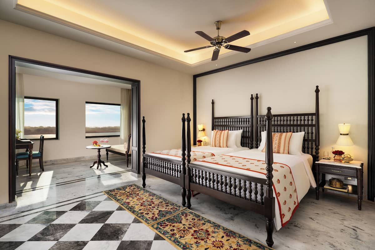 A four-poster bed with a canopy, a ceiling fan, a marble floor with a patterned rug, and a view through an open door.