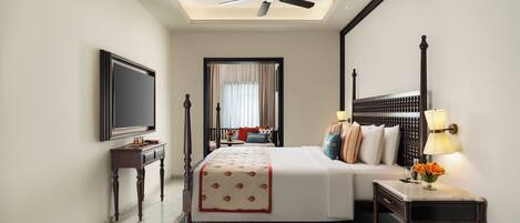A hotel room with a bed, a desk, a television, a ceiling fan, and a window with curtains.