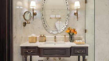 A bathroom with a large mirror, two wall-mounted lights, a sink with a towel rack, and a glass shower enclosure.