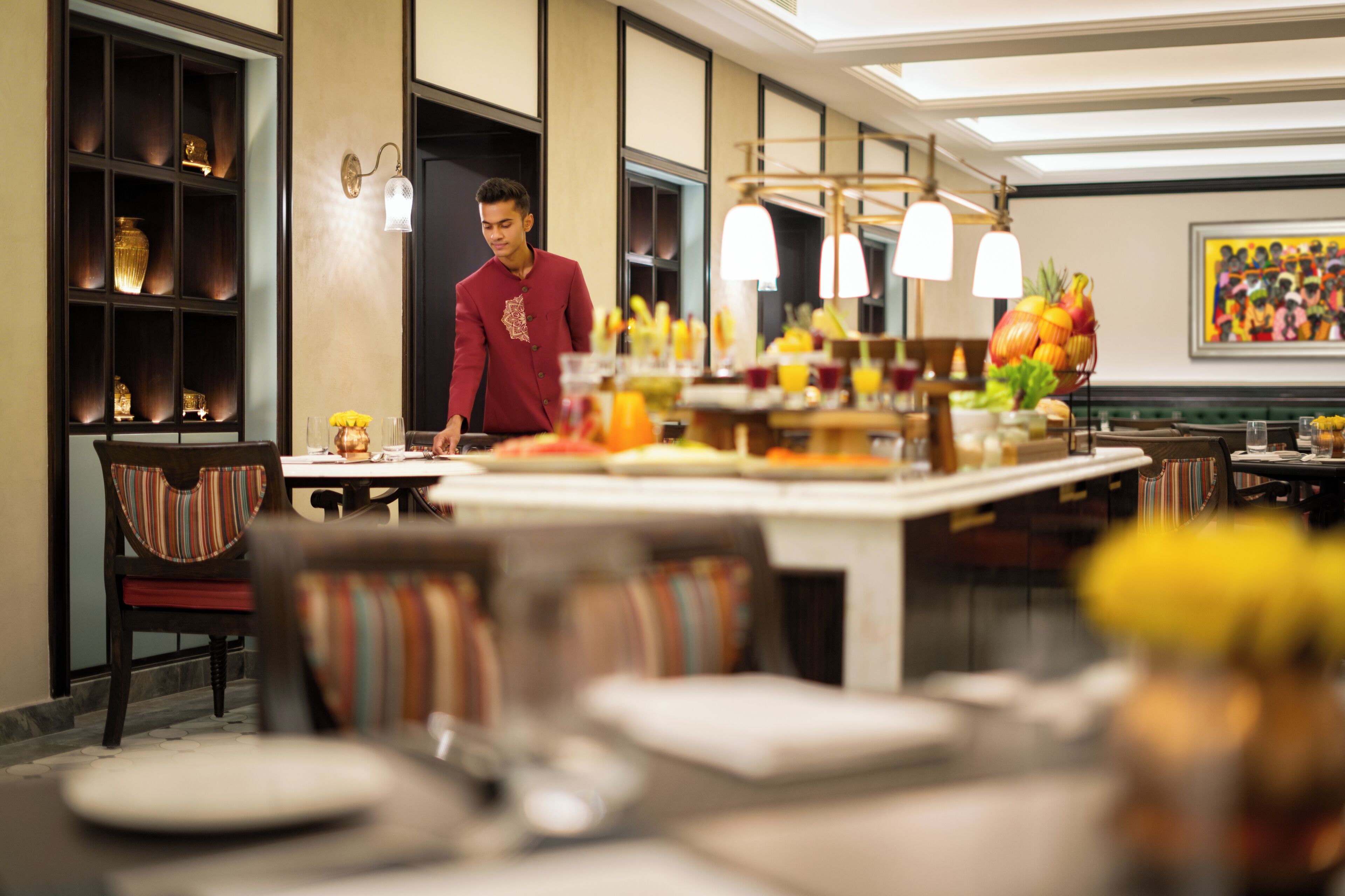 Un restaurante con un camarero, mesas con platos y una pared decorativa.