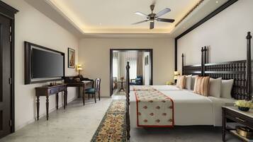 A hotel room with a large bed, a desk with a flat-screen TV, a ceiling fan, and a view of the hallway.