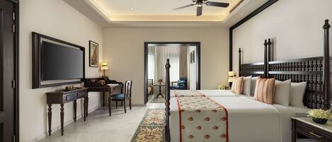 A hotel room with a large bed, a desk with a flat-screen TV, a ceiling fan, and a view of the hallway.
