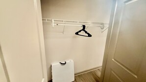 Een inloopkast met een wit opbergmeubel, een kledingroede en een witte koffer.