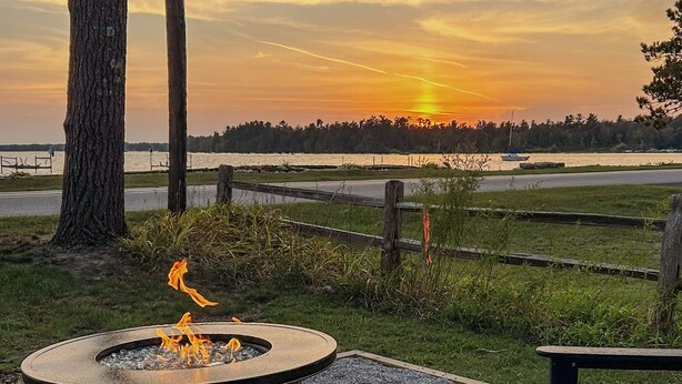 A fire pit with chairs, a gravel area, and a view of the sunset over a body of water. - Charming Lakefront Cottage (Bear Lake)