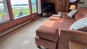 A cozy living room with a large window, a flat-screen TV, and a fireplace. - Charming Lakefront Cottage (Bear Lake)
