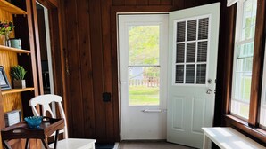A room with wooden walls, a white door, a bench, a chair, and a table. - Charming Lakefront Cottage (Bear Lake)