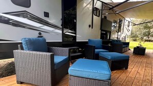 An RV with a covered deck featuring wicker furniture and a grill area. - The Bear Retreat at Venus (Highlands County)