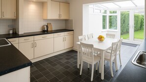 A modern kitchen with white cabinets, a black countertop, and a dining area with a white table and chairs. - Prime 4BR Reading House & Free Parking (Reading)