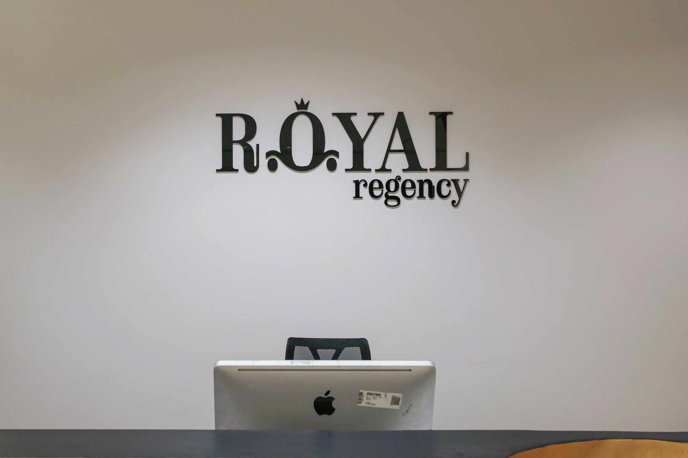 Pared blanca con el texto 'ROYAL Regency' y una computadora portátil sobre un escritorio.