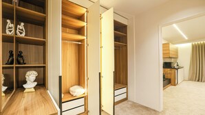 A walk-in closet with wooden shelving and drawers, a small seating area with a cushion, and a kitchenette in the background. - Royal Regency Hotel EG (New Cairo)