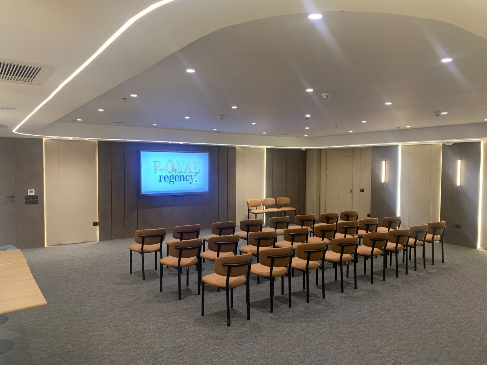 A conference room with a large screen displaying 'ROYAL regency' and rows of chairs arranged for a meeting.