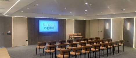A conference room with a large screen displaying 'ROYAL regency' and rows of chairs arranged for a meeting.