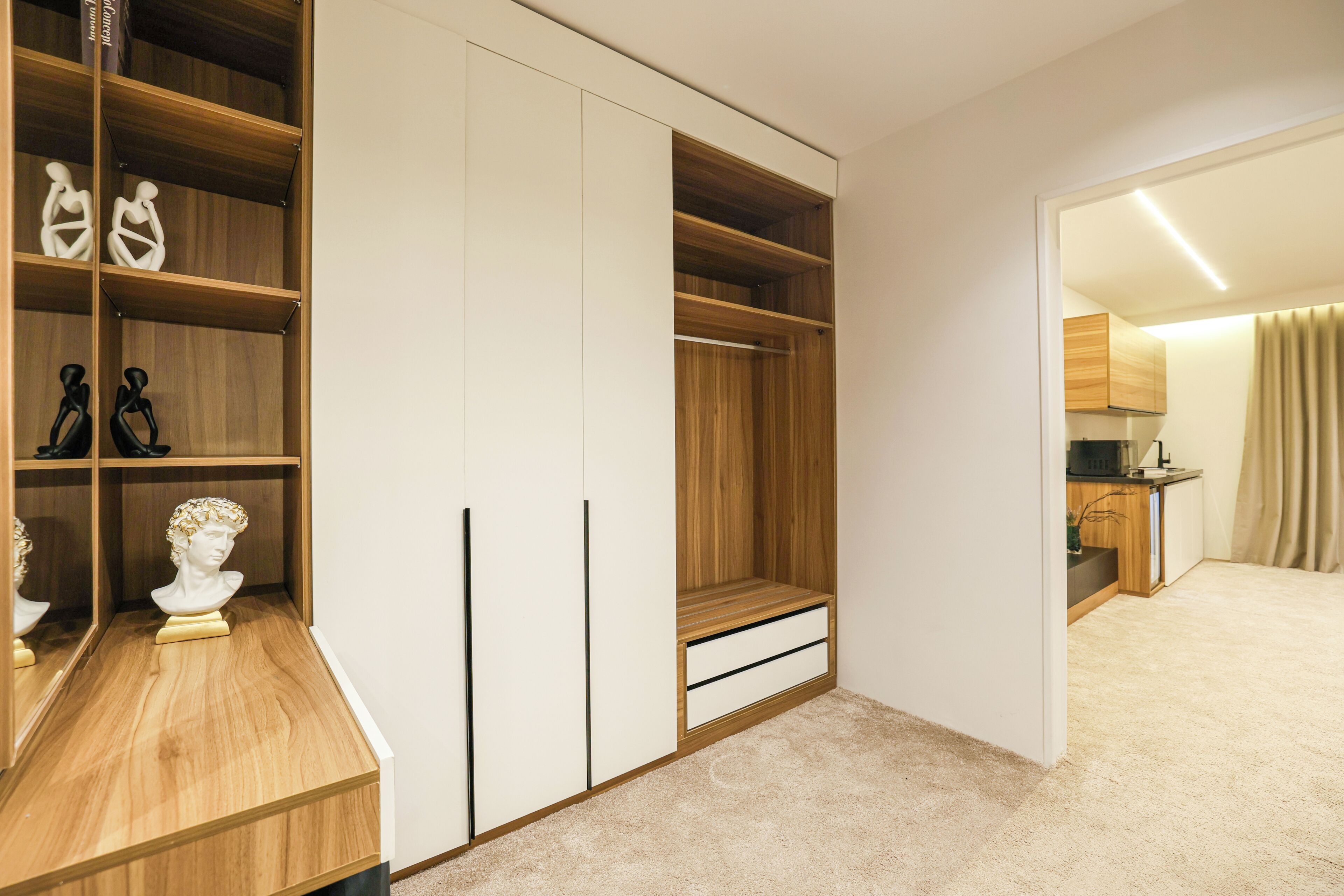 A walk-in closet with wooden shelving and a mirrored section, a white door, and a carpeted floor.