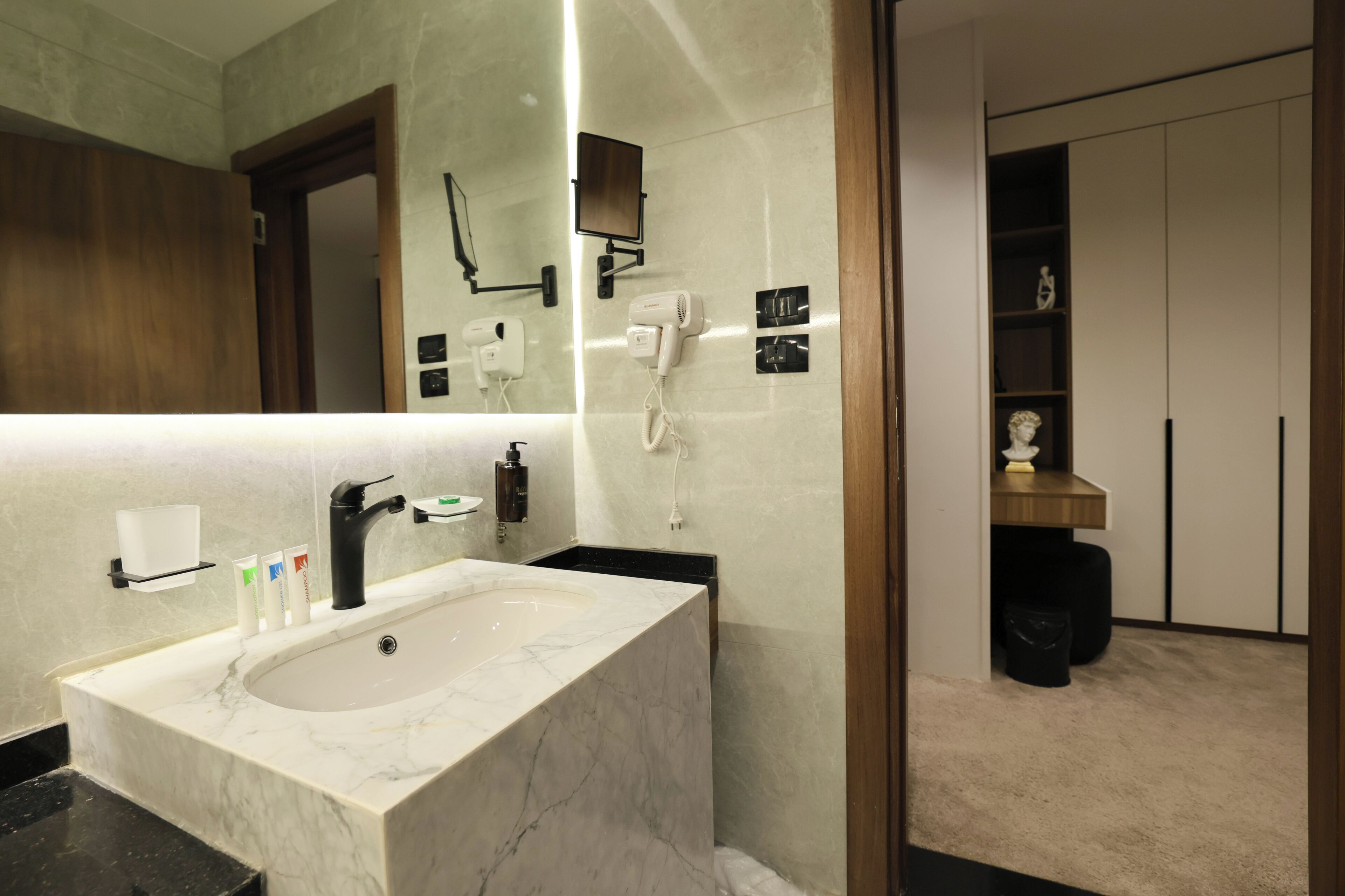A modern bathroom with a marble sink, a mirror, a hairdryer, and a vanity with a small statue.