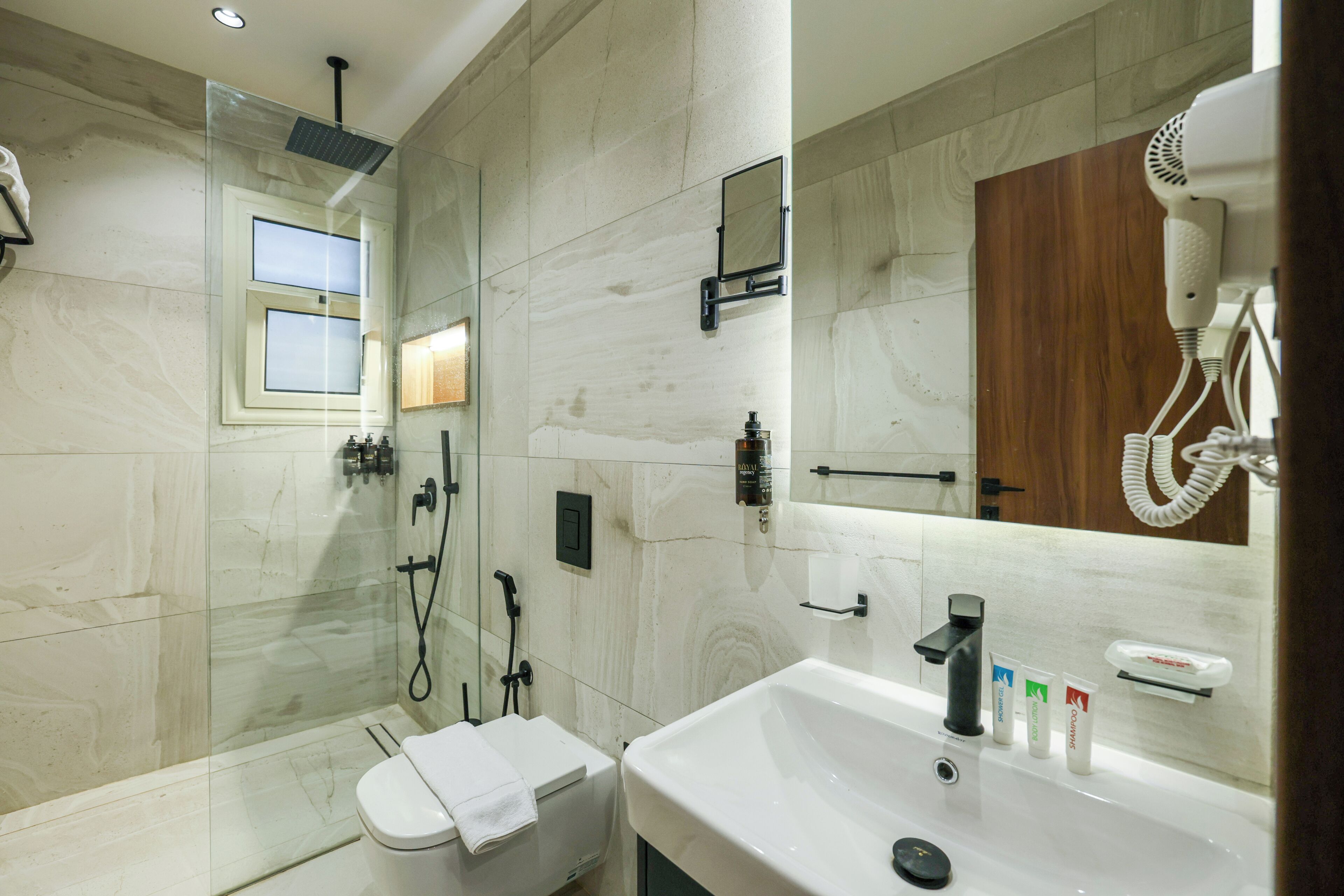 A modern bathroom with a glass-enclosed shower, a white sink, and a hairdryer mounted on the wall.