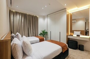 A modern hotel room with a bed, bedside table, mirror, and a small desk with a lamp.