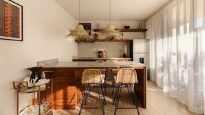 Una cucina moderna con isola centrale, sgabelli da bar, luci a sospensione e vista sull'area soggiorno.