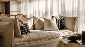 Un divano color beige con cuscini decorati in una stanza con tende leggere.