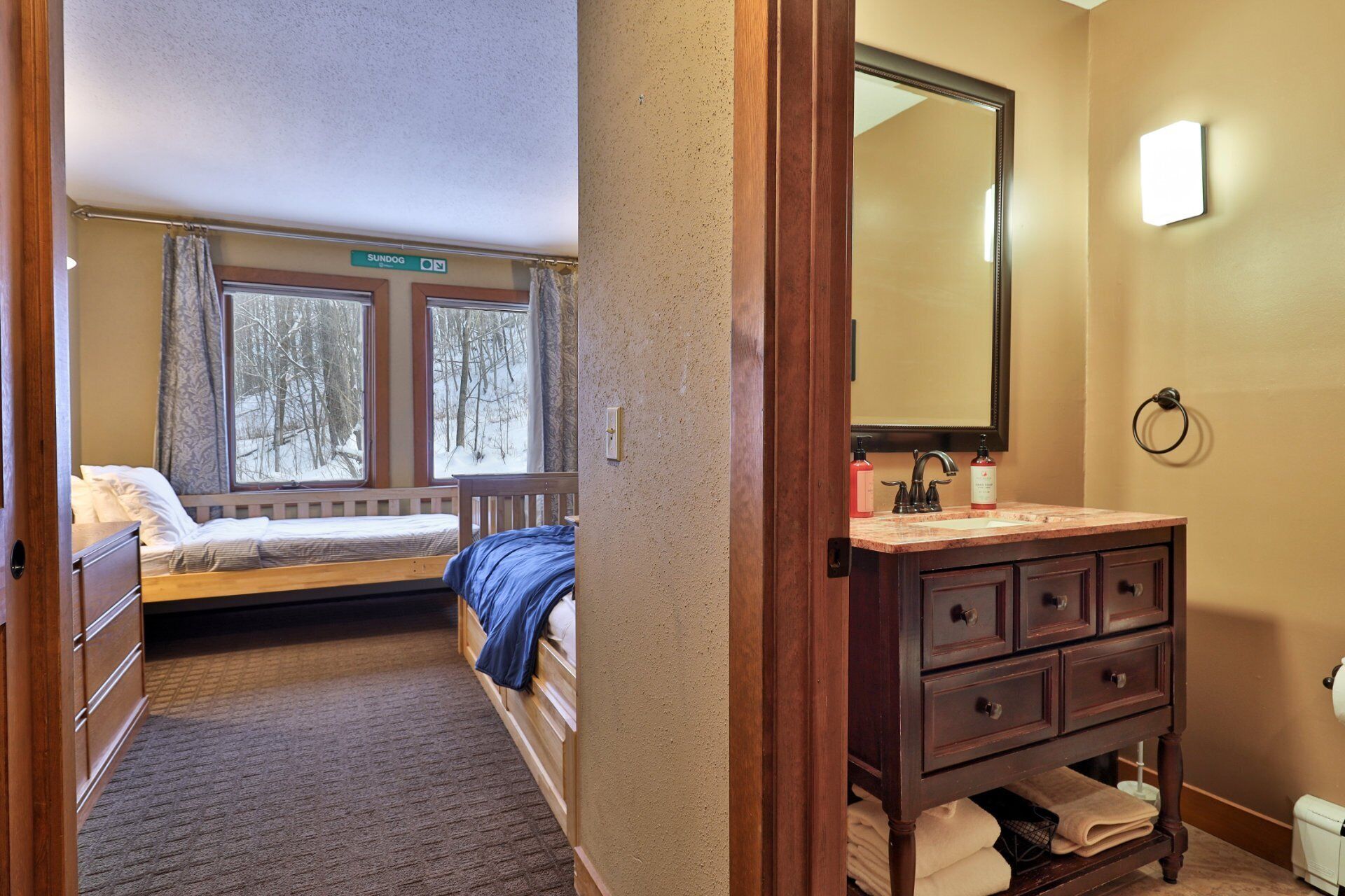Een hotelkamer met een bed, een badkamer met wastafel en spiegel, en een raam met uitzicht op bomen.