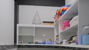 Cocina compacta con armarios blancos, un lavabo y una encimera. Hay estantes con diversos objetos, incluyendo una botella de jabón para manos y un recipiente azul.