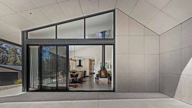 A modern interior with a large glass door leading to a dining area, a fireplace, and a kitchen visible through the glass.