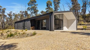 A modern building with large glass windows and a flat roof, surrounded by trees and gravel.