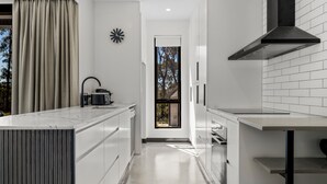 A modern kitchen with white cabinetry, a stainless steel range hood, and a window with a view of trees.