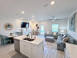 A modern kitchen with white cabinetry, a central island with a sink, and a dining area with a table and chairs.