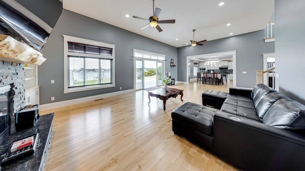 A spacious living room with a large black leather sofa, a wooden coffee table, and a fireplace. There are two ceiling fans and a large window with blinds. - WATER FRONT PROPERTY WITH PRIVATE BOAT DOCK (Ferndale)