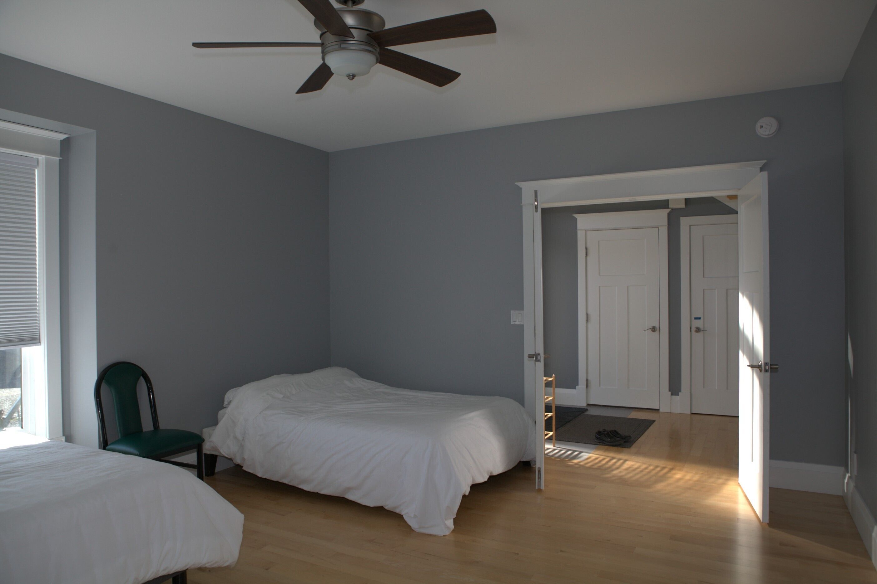 Een slaapkamer met een bed, een stoel, een plafondventilator en een deur naar een andere kamer.