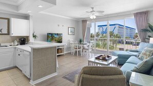 A modern living room with a dining area, a kitchen, and a balcony with a view of a building labeled "The Dal." - Destin West Gulfside 305 ~ Ocean Views ~ Beach Service (Fort Walton Beach)