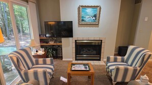 A living room with a fireplace, two striped armchairs, a sofa, a coffee table, and a flat-screen TV. - Creek Comfort! Charming sleeps 6 condo in lovely Bellaire. Short drive to skiing (Bellaire)
