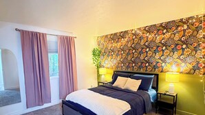 Un dormitorio con una cama grande, una mesita de noche, una lámpara de pared y un papel tapiz floral.